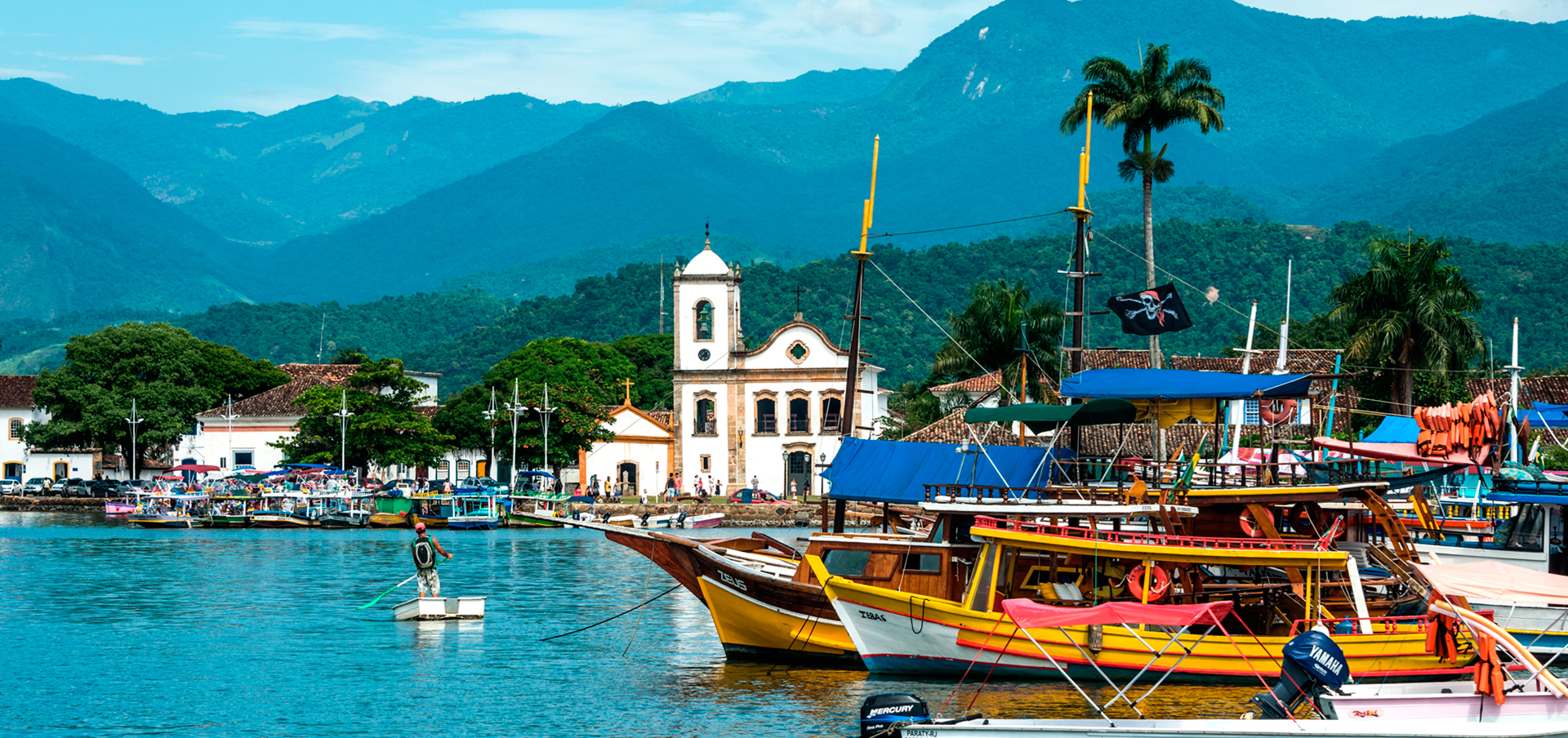 Vista aérea do centro histórico de Paraty, RJ, com barcos coloridos e a Serra do Mar ao fundo